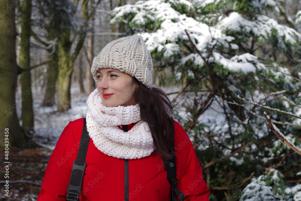 Woman walking in the woods in winter outdoors. Girl in red clothes and white hat hiking in snowy forest. Frosty sunny day in December. Female lifestyle portrait Woman walking in the woods in winter outdoors. Girl in red clothes and white hat hiking in snowy forest. Frosty sunny day in December. Female lifestyle portrait