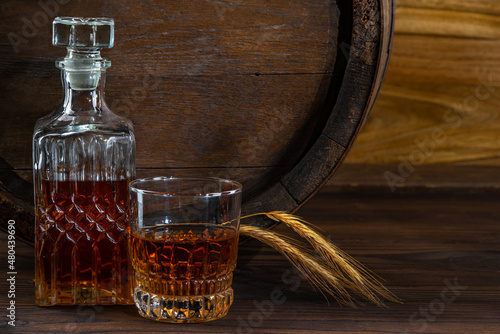 Glass decanter with whiskey, brandy on a vintage background of a rustic oaken barrel. Alcoholic beverage. Still life in the old style