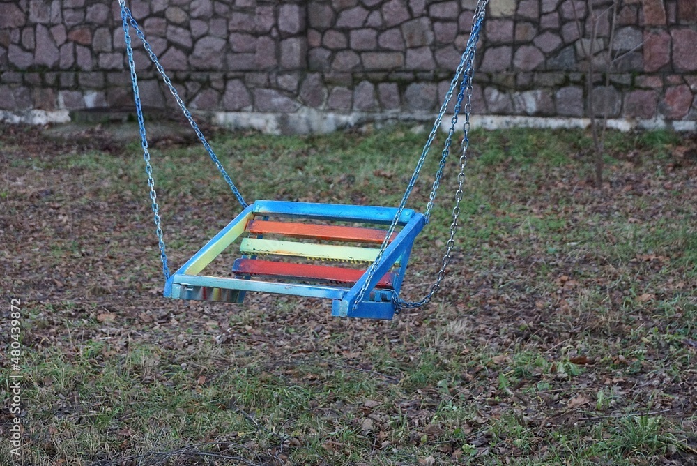 one colored child seat on a swing with metal chains in a park on the street