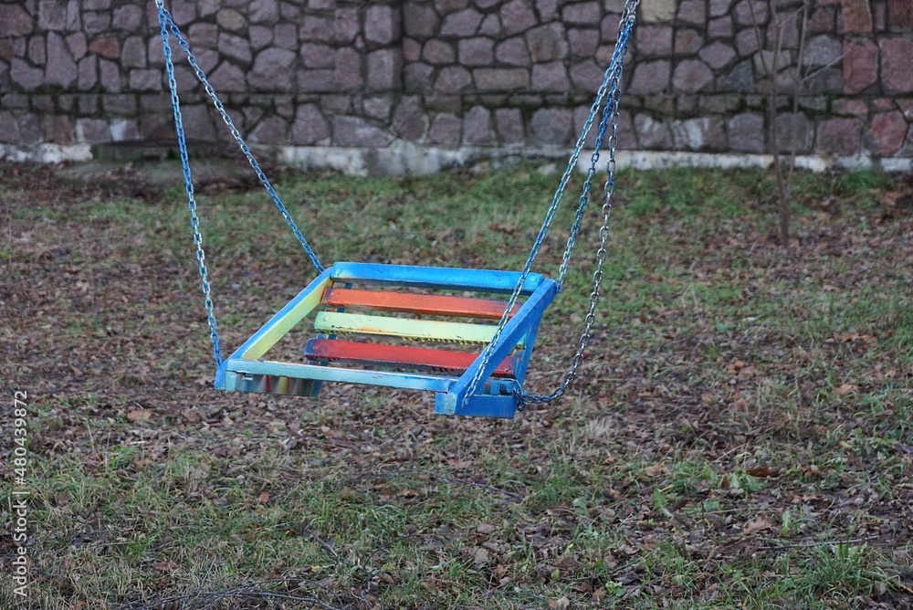 one colored child seat on a swing with metal chains in a park on the street one colored child seat on a swing with metal chains in a park on the street