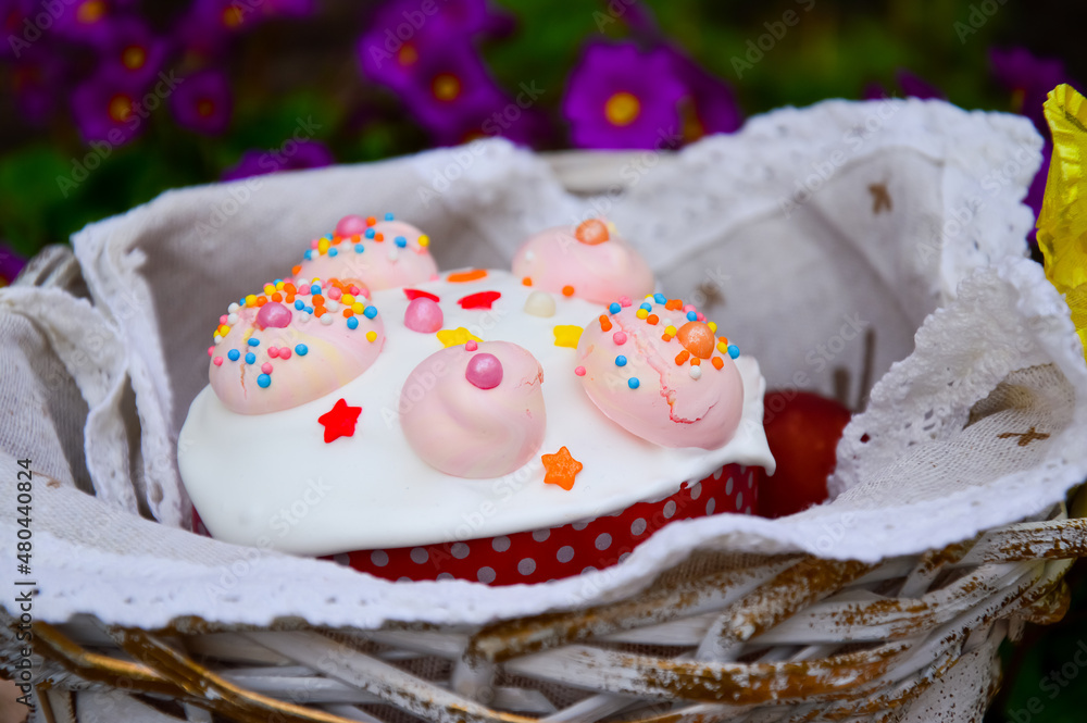 Happy Easter. Easter basket with a cake with white icing and pink meringue. Homemade pastries for the Easter holiday on the background of purple primrose flowers Happy Easter. Easter basket with a cake with white icing and pink meringue. Homemade pastries for the Easter holiday on the background of purple primrose flowers