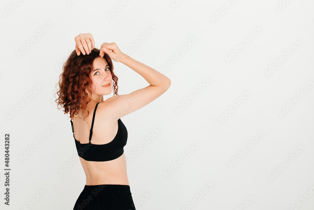 Beautiful curly redhead woman posing in black sportswear, turning around to look at the camera, on white studio background Beautiful curly redhead woman posing in black sportswear, turning around to look at the camera, on white studio background