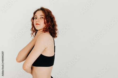 Young sensual woman with curly hair looking at the camera, holding herself with her arms, standing over white background