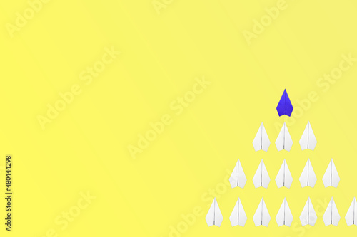 blue paper plane leading among a white planes on yellow background. Business competition and Leadership concept