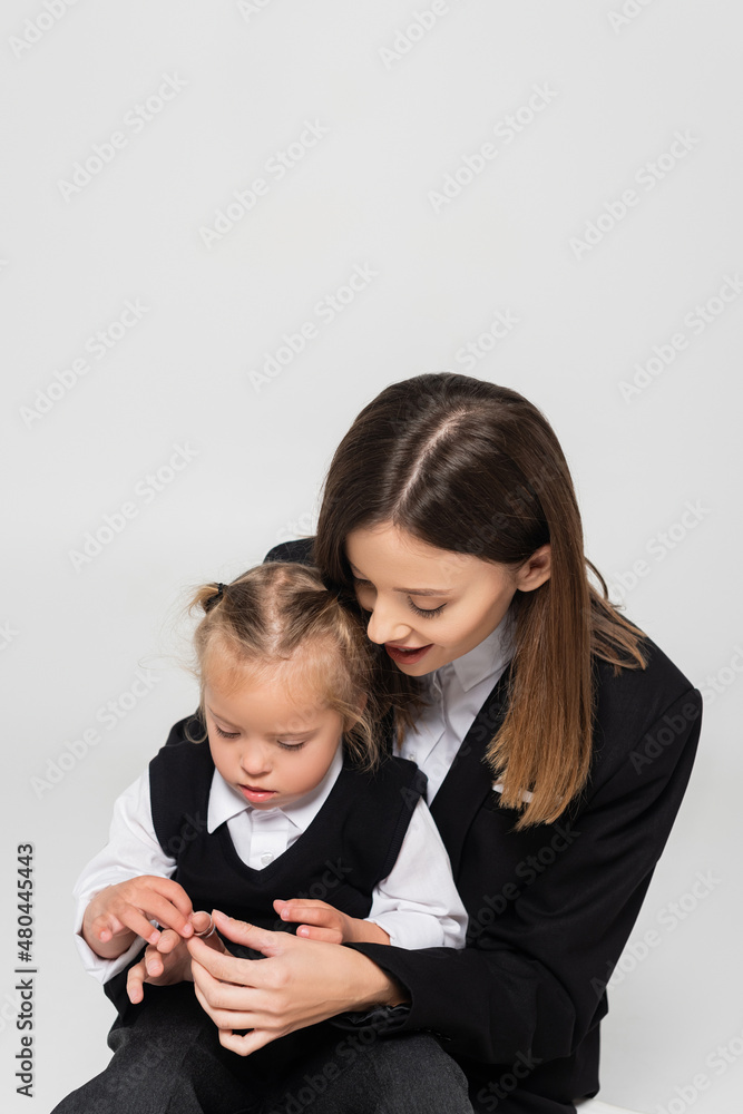 cheerful mother touching hand of child with down syndrome isolated on grey.