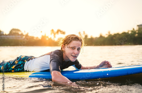 Portrait of a teen boy with Dental braces floating on surfboard. He is smiling. Happy childhood and active vacation time concept.