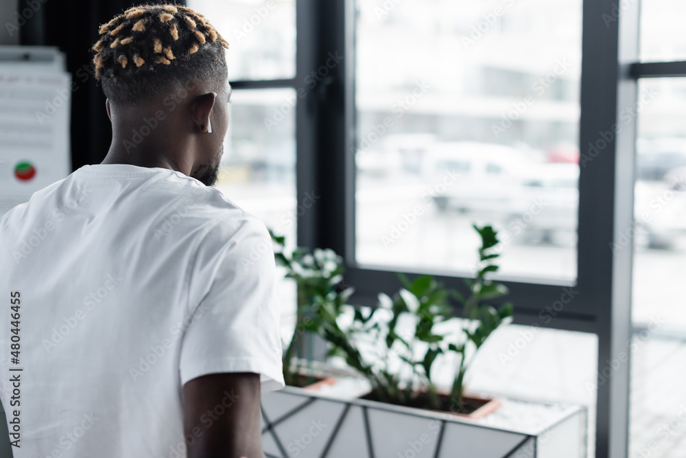 back view of african american man with trendy hairstyle listening music in earphone in office. back view of african american man with trendy hairstyle listening music in earphone in office.