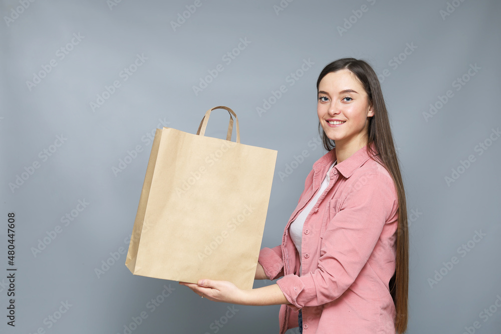 Attractive and smiling young girl in pink blouse holding blank paper bag with space for logo or design. Attractive and smiling young girl in pink blouse holding blank paper bag with space for logo or design.