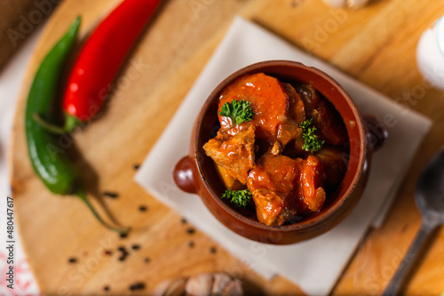 meat goulash in a ceramic pot on a wooden background