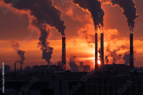 Smoke from heating station in big city during winter season at sunset. Smokestack pipes emitting co2 from coal thermal power plant into atmosphere. Air pollution and emission ecology problem concept