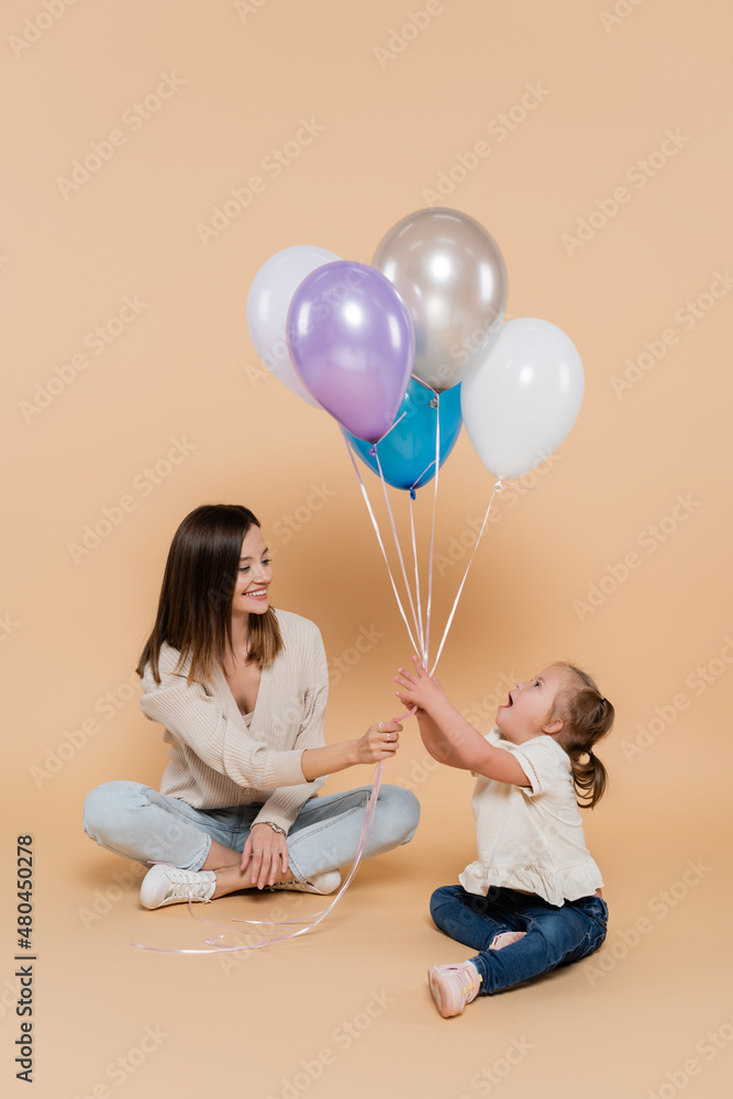 positive woman giving colorful balloons to girl with down syndrome on beige.