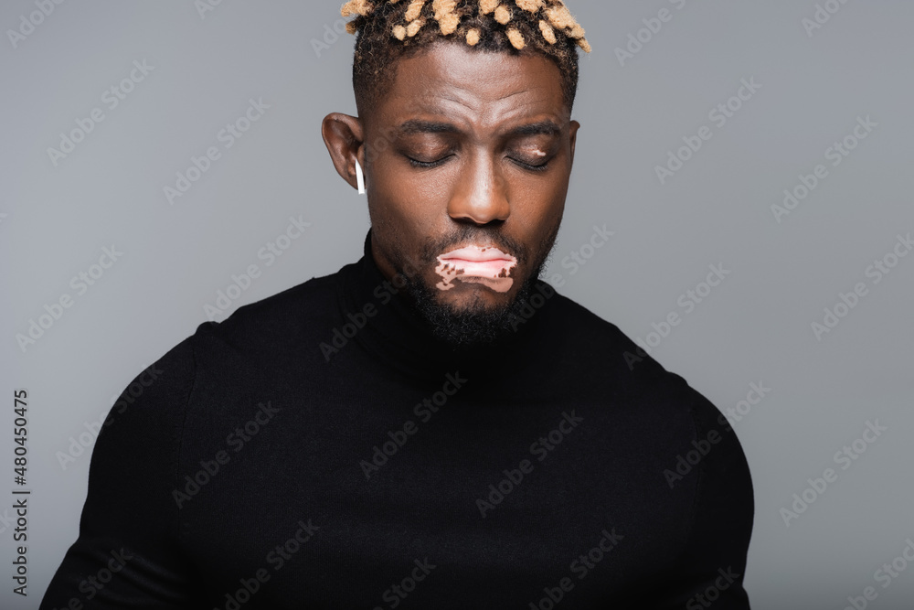 Fototapeta premium african american man with vitiligo skin listening music in earphone with closed eyes isolated on grey.