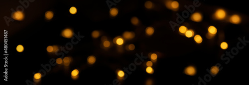 Banner of Defocused bokeh lights on black background, an abstract naturally blurred backdrop for Valentine Day or birthday party. Festive light texture. Yellow, orange garland in blur. Overlay effect
