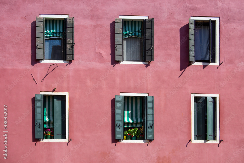 six shuttered venetian windows on a canal side building with bright pink paintwork