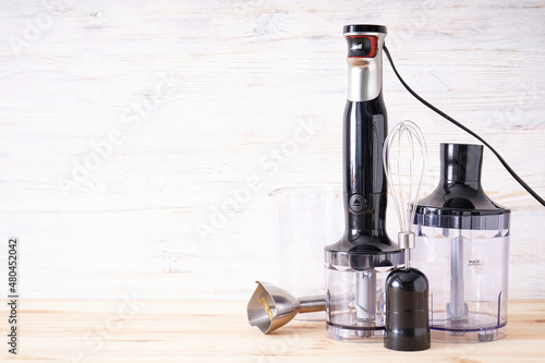 Black plastic electrical hand blender with stainless steel body and accessory on the wooden background, place for text.