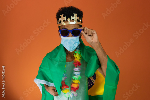 Black man in costume for carnival with brazil flag and pandemic mask isolated on orange background. African man in various poses and expressions. © Andre Nery