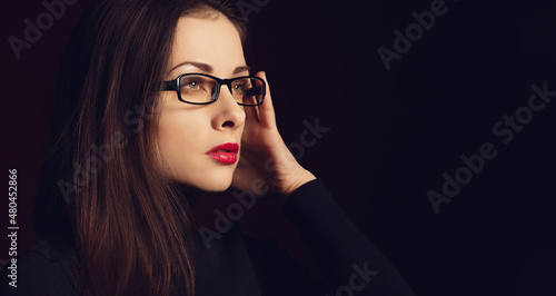 Business thinking serious woman in eye glasses looking with hand near the face on dark shadow background with empty copy space. Closeup profile