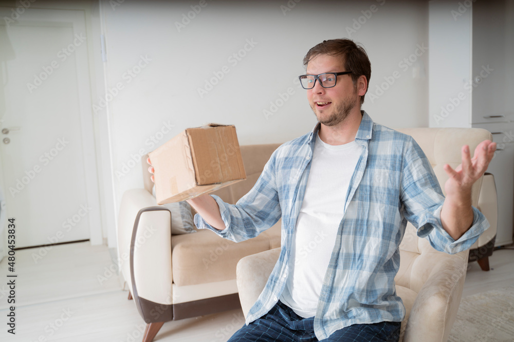 Happy middle-aged man unpacking delivery box, sitting at home interior. Satisfied customer cheerful man opening package, happy customer opens a cardboard box with an order in an online store