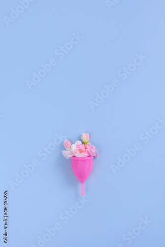 Menstrual cup and sakura flowers on blue background. Concept of alternative methods of feminine hygiene. Copy space, vertical banner © ClareM