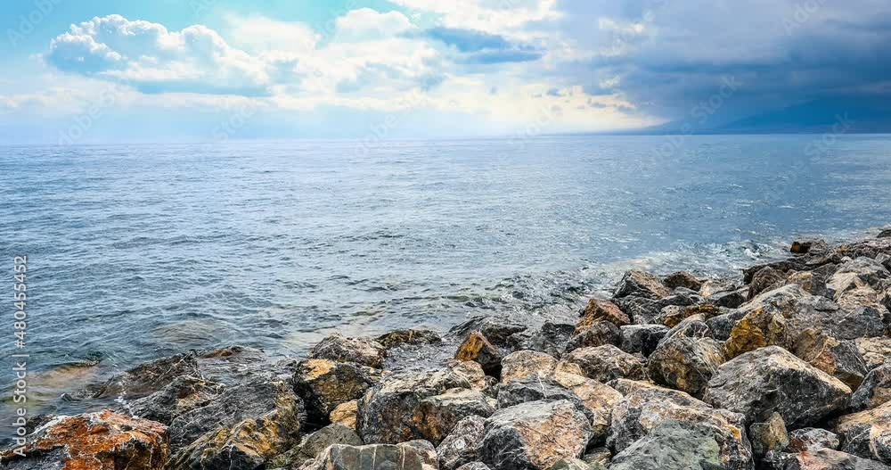 Sailimu Lake natural scenery in Xinjiang, China. Lake water lapping stones on shore. Clear lake water and rocks with mountain under blue sky. Sailimu Lake natural scenery in Xinjiang, China. Lake water lapping stones on shore. Clear lake water and rocks with mountain under blue sky.
