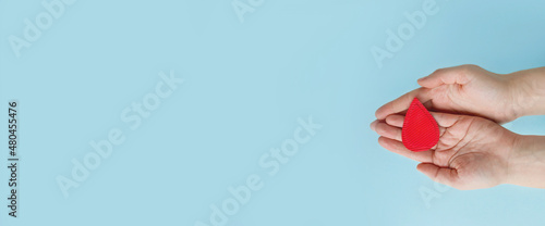 Concept of give blood donation, blood transfusion. Hands woman hold drop of blood on blue background. World hemophilia day.