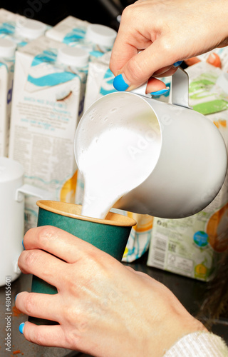 Barista pours frothy whipped cream into a green paper coffee cup.