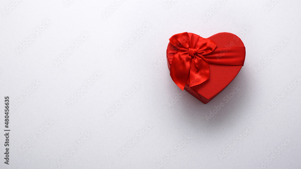 Red heart-shaped gift box with a red ribbon on the right side on a white background. Happy Valentine's Day. Anniversary. Top view flat lay copy space. Red heart-shaped gift box with a red ribbon on the right side on a white background. Happy Valentine's Day. Anniversary. Top view flat lay copy space.
