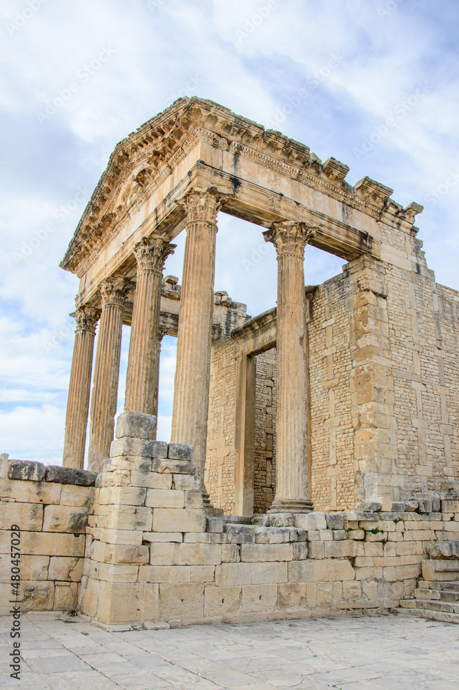 Portico of the ruined temple of Jupiter in the ancient roman city of Dougga in Tunisia, Africa. Blue sky with clouds, old yellow, grey and brown stone walls and columns