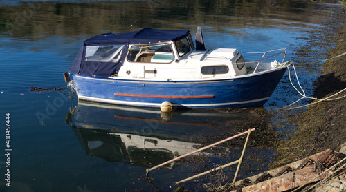 Small boats moored in a Cornish harbour, bright blue water with reflections & shadows