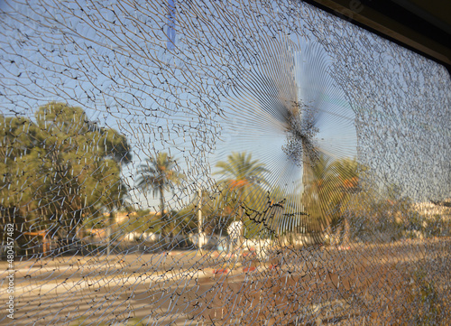 Defocused view of a palm trees and road in Tunisia, Africa, through a broken glass of the train window. Blue sky, grey asphalt, green leaves and radial cracks on the glass.