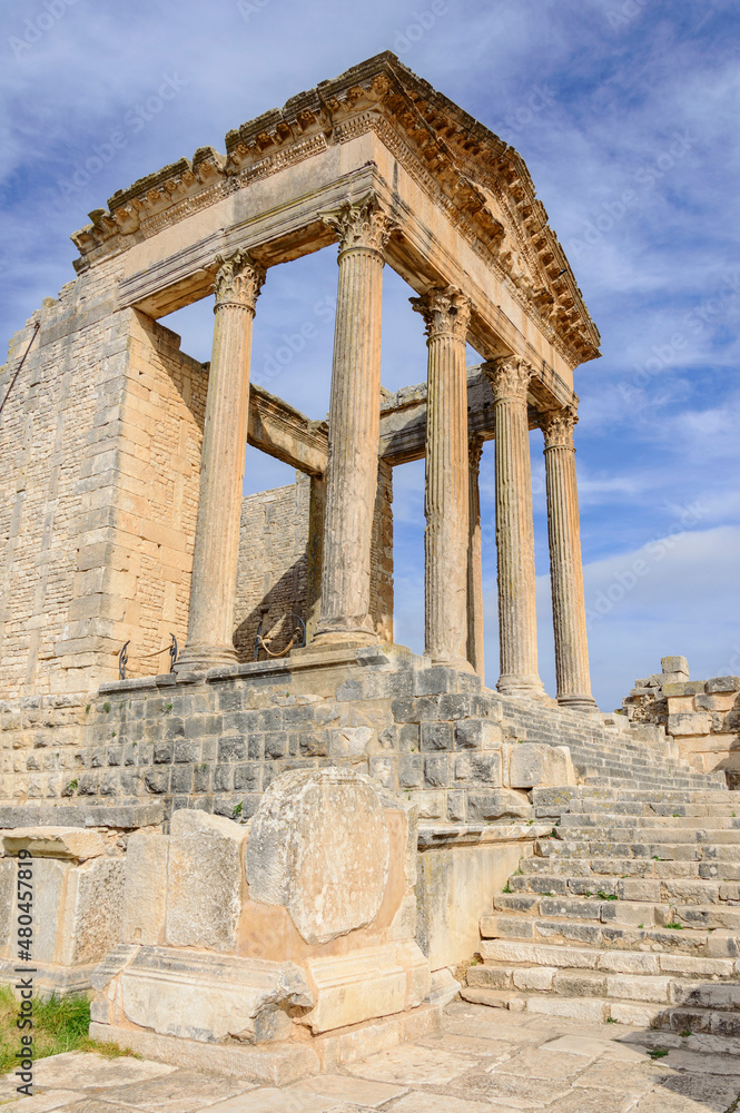 Fototapeta premium Temple of Jupiter and ancient roman ruins of Dougga in Tunisia, Africa in the sunny afternoon. Blue sky with clouds, old yellow, grey and brown stone walls and columns 