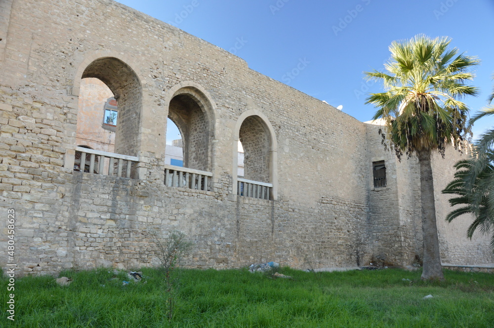 Old town medina walls in monastir, Tunisia, Africa. Ancient yellow and grey stone walls with arches, blue sky, green grass, palm trees