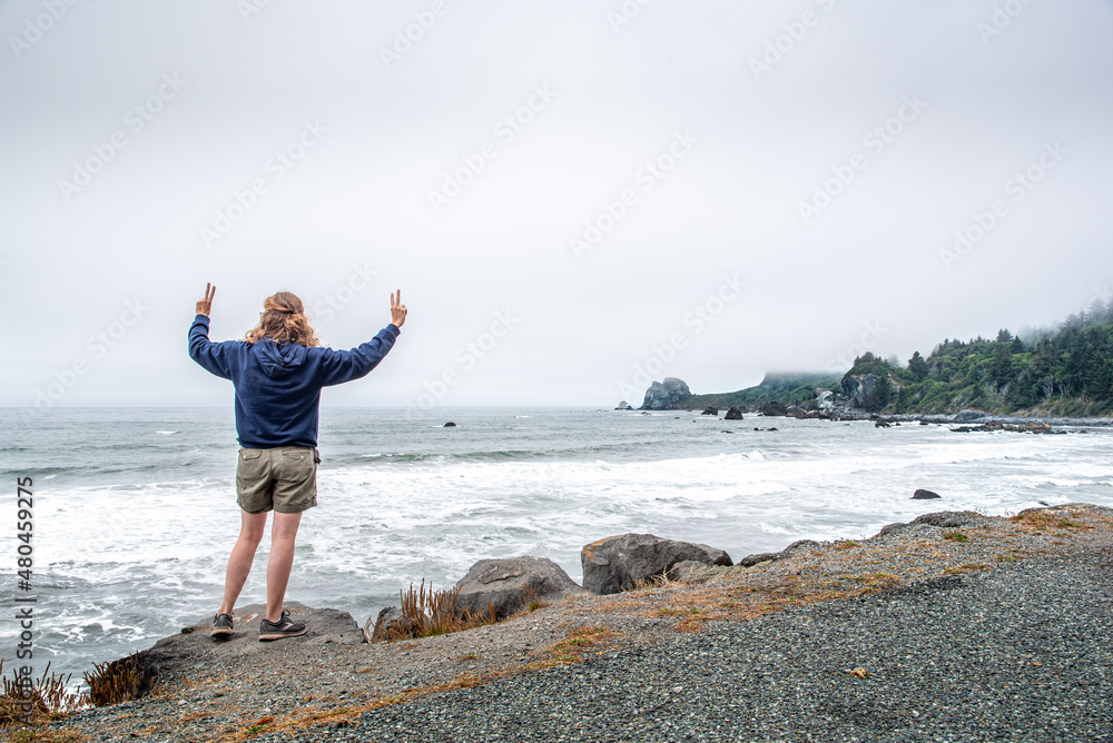 Girl Standing Seaside on Ocean Cliff with Peace Signs and Arms Out in the Wind