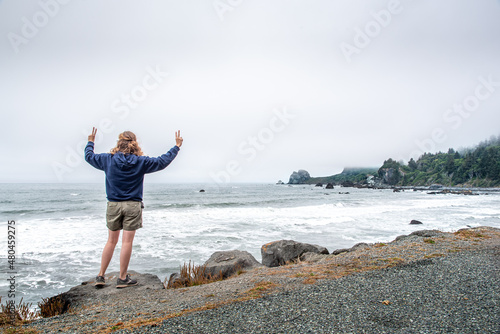 Girl Standing Seaside on Ocean Cliff with Peace Signs and Arms Out in the Wind photo