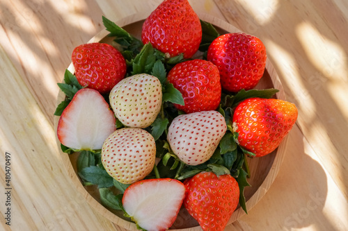 Delicious Red and White Strawberry in wooden Basket under Sun Light and Shadow of leaf in the garden.Hula strawberry in basket.