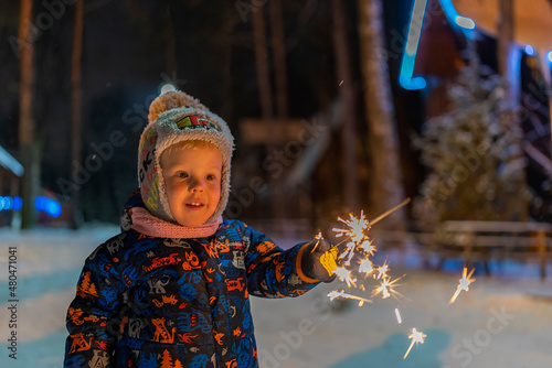 little boy light a winter sparkler on the background with Christmas lights.