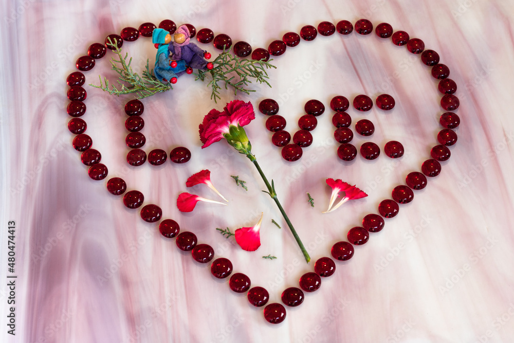 Red carnation inside a heart of red glass beads spelling LOVE with gender neutral elves hugging Red carnation inside a heart of red glass beads spelling LOVE with gender neutral elves hugging