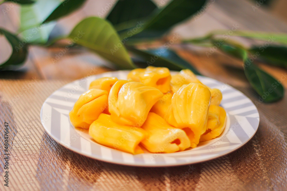 Jackfruit is fresh in a white plate, placed on a wooden table with jackfruit branches. Jackfruit is fresh in a white plate, placed on a wooden table with jackfruit branches.