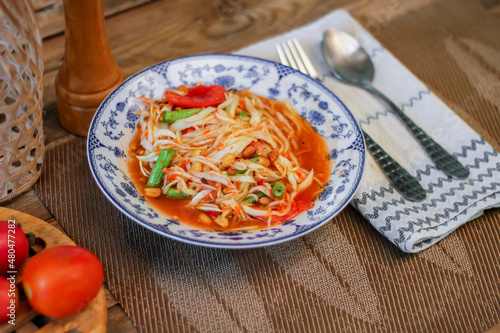 Thai papaya salad or what we call " Somtum " in Thai. The famous local Thai street food dish with the taste of hot and spicy on wood table.