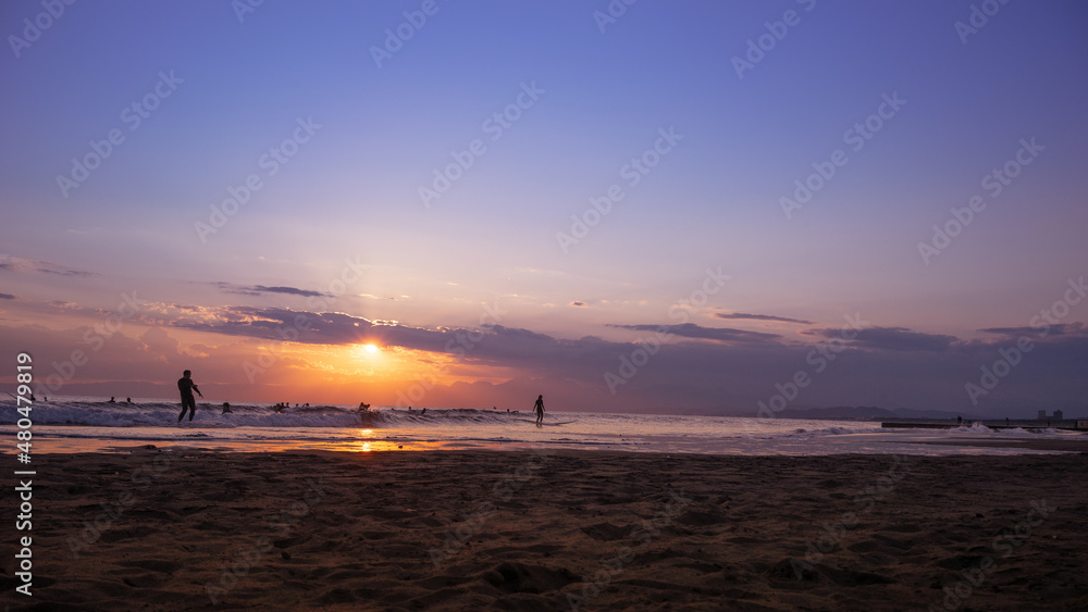 Naklejka premium 日本の綺麗な夕日と海岸の景色 サーフィンを楽しみむ人のシルエット