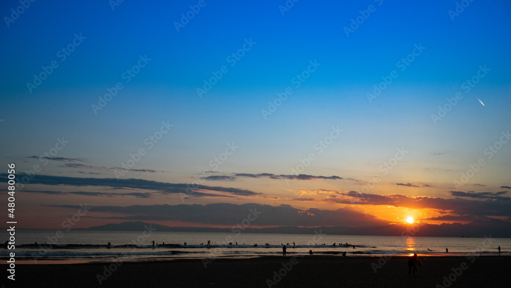 Fototapeta premium 日本の綺麗な夕日と海岸の景色 サーフィンを楽しみむ人のシルエット