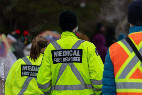 Medical first responders walking along a road wearing black wool stocking caps, yellow reflective coats with the medical first responder in grey letters and across. The EMT is carrying a first aid kit © Dolores  Harvey