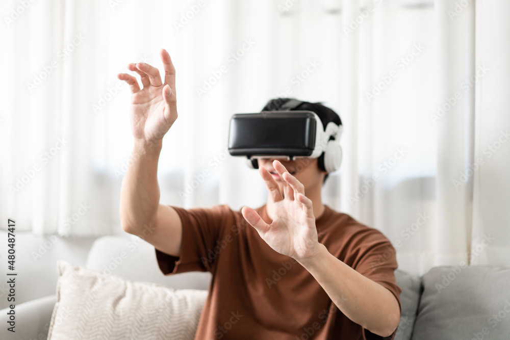 Technology Concept The man with his brown T-shirt and light blue jeans wearing a virtual reality headset while sitting on the sofa Technology Concept The man with his brown T-shirt and light blue jeans wearing a virtual reality headset while sitting on the sofa