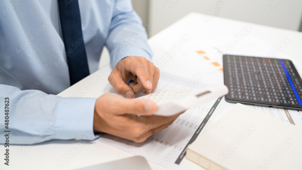 Working Man Conept The male officer sitting at his desk, holding the calculator, and pressing it Working Man Conept The male officer sitting at his desk, holding the calculator, and pressing it