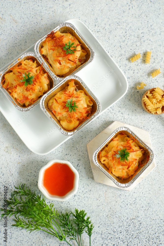 selective focus of  baked macaroni and cheese  in aluminium foil cup against white background 