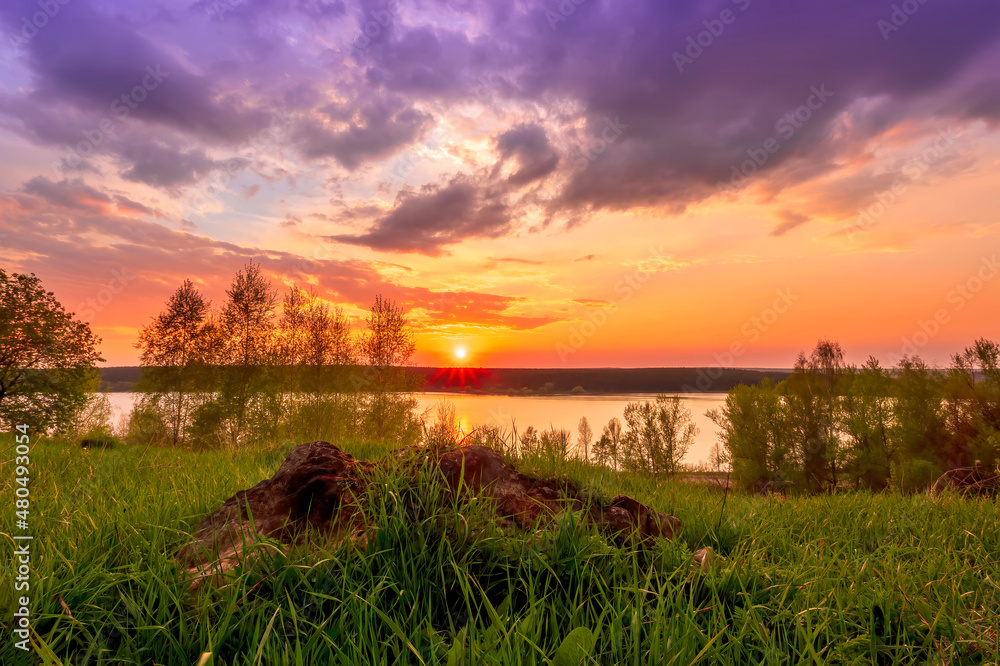 Beautiful scenic view at nice landscape on a beautiful lake and colorful sunset with reflection on water with green gras on foreground and glow on a background, spring season landscape