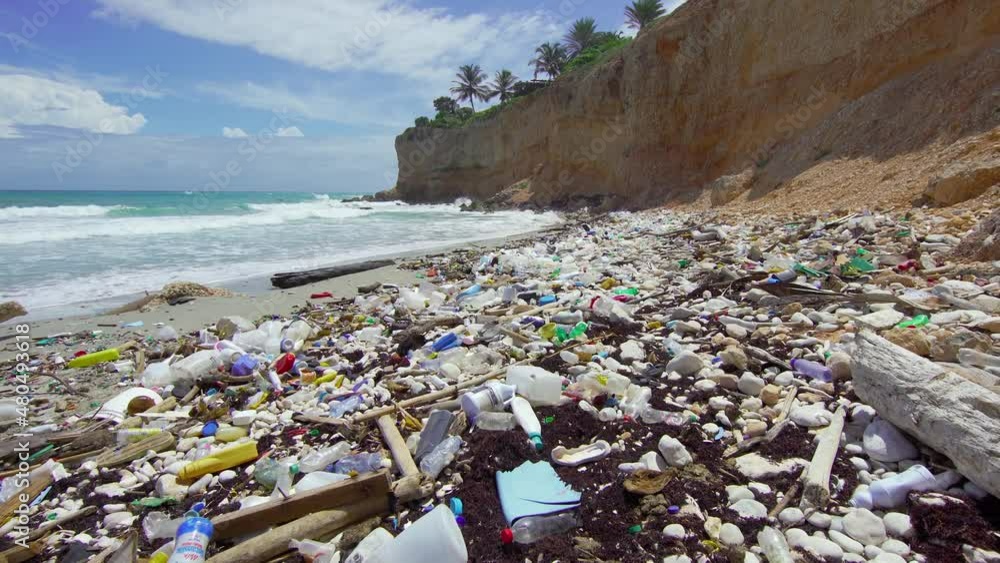 Tropical peninsula beach covered in plastic waste. Ocean waves wash
