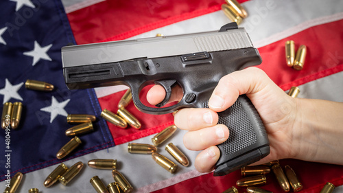 Hand holds gun against American flag. Hand gun and bullets, concept of USA firearms tradition, second amendment and gun control. 9mm modern handgun.