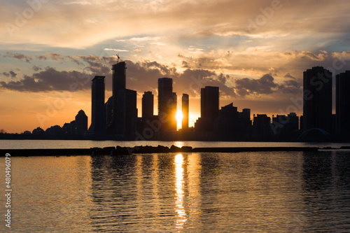 Amazing sunset over sityscape. Cloudy sky with sun rays, water reflection. City modern buildings