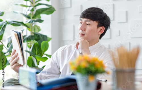 Portrait studio shot of Asian professional successful male businessman employee in formal shirt with necktie sitting look at camera at working desk with computer monitor keyboard mouse and stationery